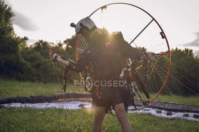 Junger Mann mit dem Gleitschirmmotor auf den Schultern macht sich bereit, bei Sonnenuntergang zu fliegen. — Stockfoto