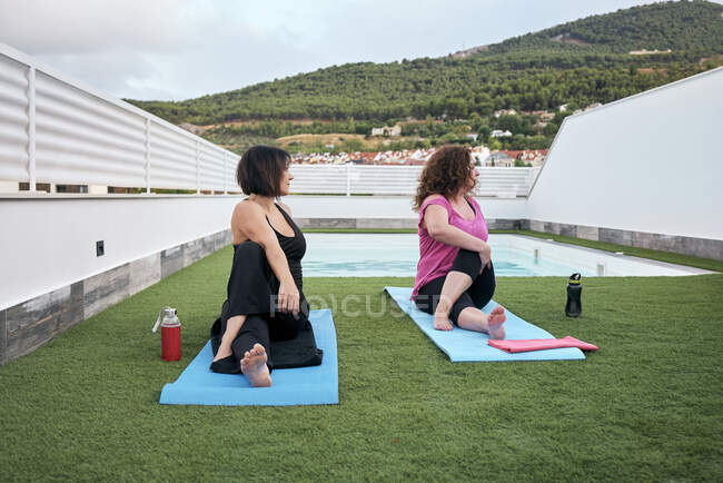Две женщины практикуют йогу на террасе дома, осанка Маричи — стоковое фото