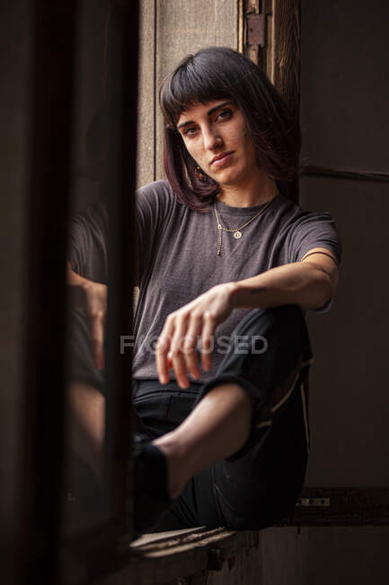 Brunette fille assise sur une fenêtre d'une vieille maison abandonnée — Photo de stock