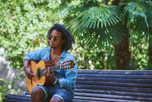 Musicista che suona la chitarra in un bel parco. E 'circondato dalla vegetazione. — Foto stock