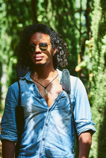 Musicista che cammina con la chitarra appesa alla schiena. Cammina in un parco con vegetazione. — Foto stock