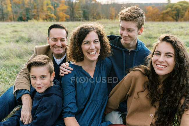 A happy family of five sitting together in a field — Stock Photo