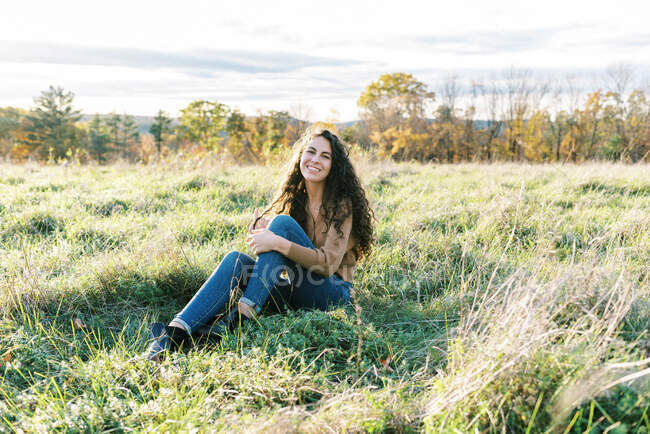 Feliz adolescente sentada en un campo de hierba alta - foto de stock