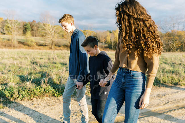 Dos adolescentes caminando con su hermano pequeño en el medio - foto de stock