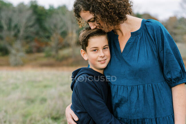 Una madre cariñosa besando a su hijo de diez años encima de su cabeza - foto de stock