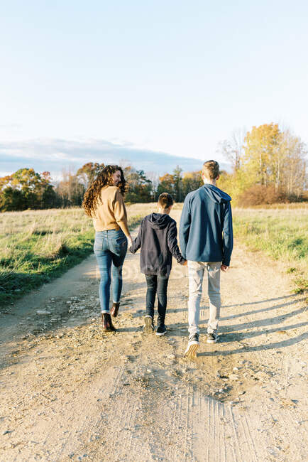 Two teenagers walking with their little brother in the middle — Stock Photo