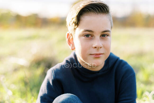 Retrato de um sério olhando menino de dez anos sentado fora — Fotografia de Stock
