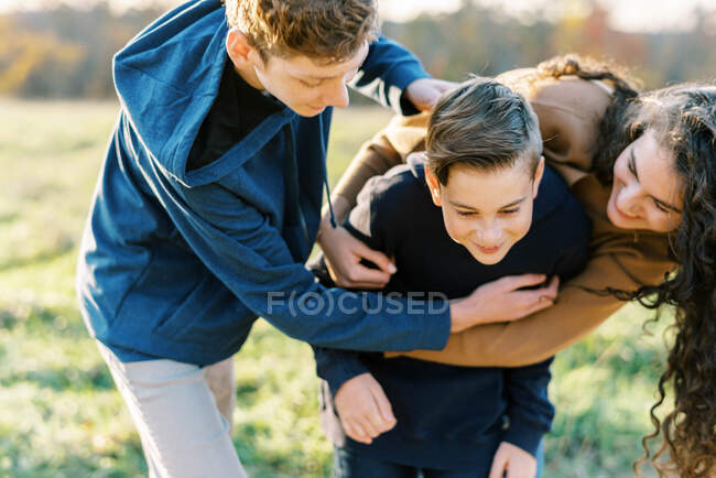 Two teenage kids hugging their kid brother tight — Stock Photo