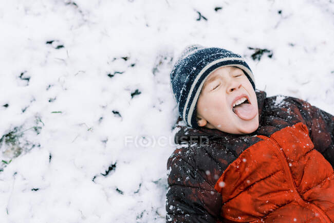 Menino deitado na neve tentando pegar flocos de neve — Fotografia de Stock