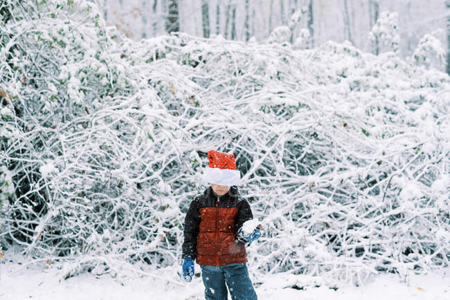 Маленький мальчик играет во время снегопада с его шляпой Санты на голове — стоковое фото