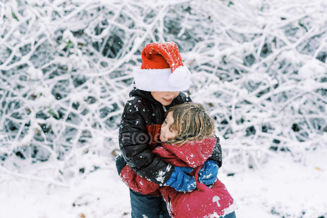 Niños pequeños jugando durante una nevada afuera usando un sombrero de Santa - foto de stock