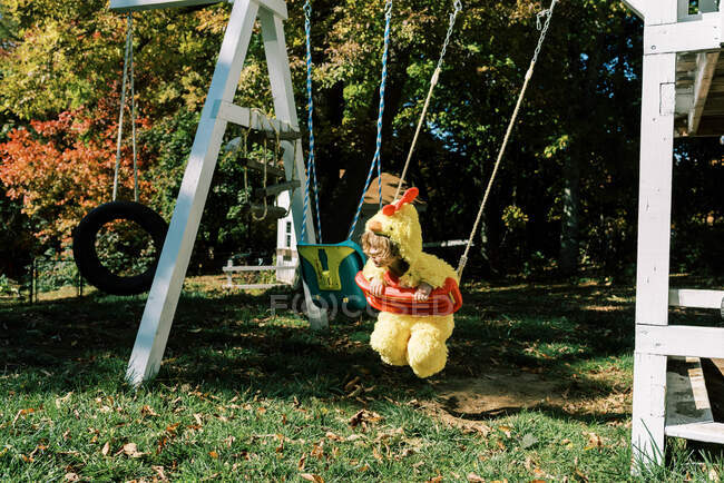 Little girl in chicken costume on a swing in fall — Stock Photo