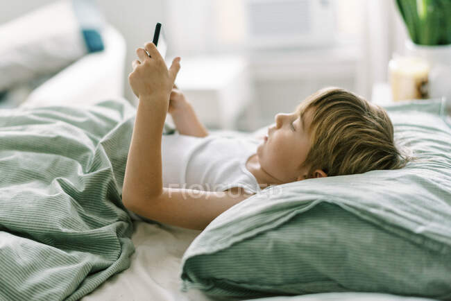 Niño despertando por la mañana jugando su tableta - foto de stock