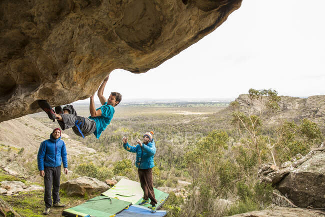 Sportlicher Mann klettert draußen auf einen Felsbrocken und entdeckt Männer — Stockfoto