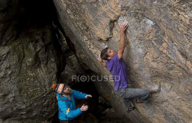 Athletic male climbs outside on a boulder with man spotting — Stock Photo