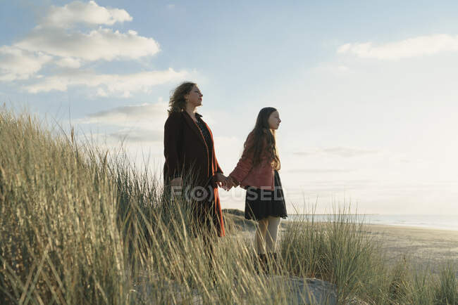 Mãe e filha em pé na praia contra vista da paisagem marinha — Fotografia de Stock