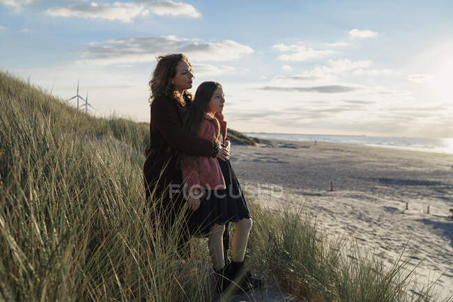 Mãe e filha em pé na praia contra vista da paisagem marinha — Fotografia de Stock