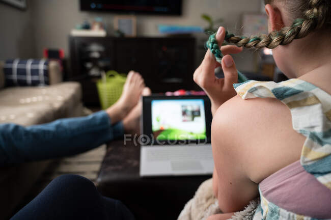 Tra ragazza giocare con capelli mentre guardando computer portatile in salotto — Foto stock