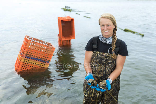 Female shellfish farmer in water holding oysters in hands — Stock Photo