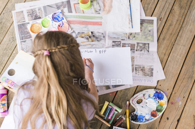 Blick von oben auf ein junges Mädchen, das draußen auf einem Holzdeck malt — Stockfoto