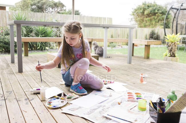 Молодая девушка рисует на деревянной палубе с котом на заднем плане — стоковое фото