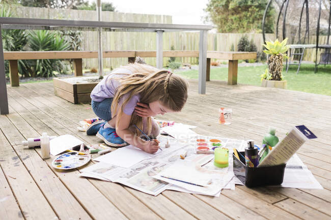 Young girl painting outside on a wooden deck — Stock Photo