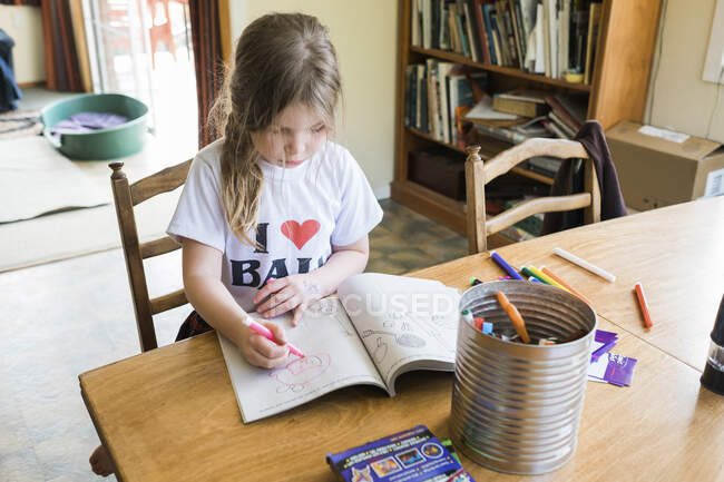 Дівчинка сидить за барвистим столом і малює — стокове фото