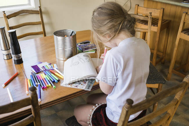 Jeune fille assise à une table de coloriage et de dessin — Photo de stock