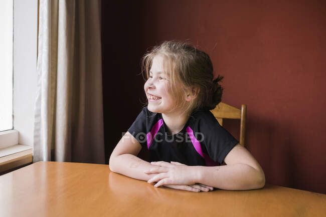 Jeune fille assise à l'intérieur à la table de la salle à manger regardant à l'extérieur — Photo de stock