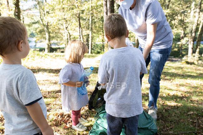 Madre raccogliendo bottiglie di plastica con i suoi figli nella foresta — Foto stock