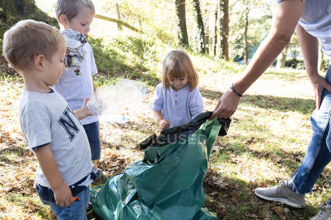 Madre recogiendo botellas de plástico con sus hijos en el bosque - foto de stock