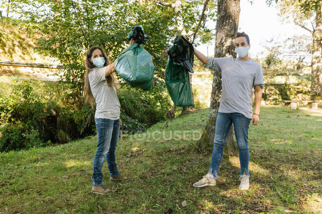 Pareja voluntaria sosteniendo bolsas de basura en una cámara con aspecto de bosque - foto de stock