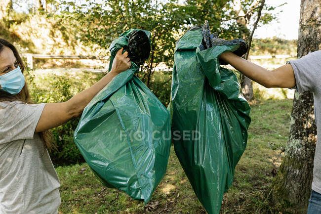 Primer plano de una pareja de voluntarios sosteniendo bolsas de basura en un bosque. - foto de stock