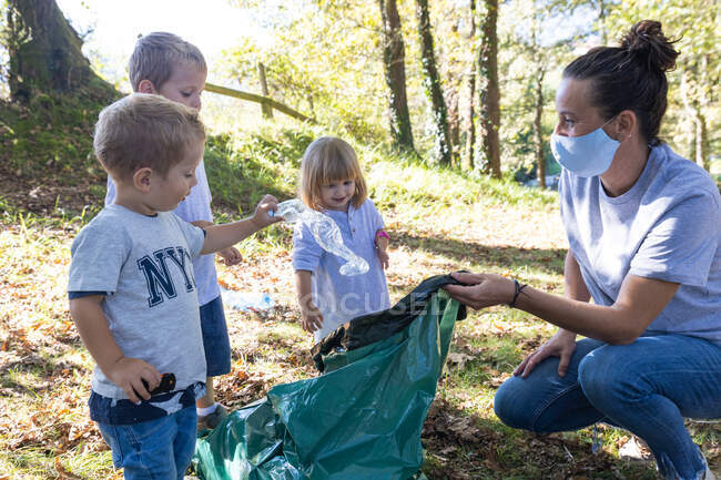 Madre raccogliendo bottiglie di plastica con i suoi figli nella foresta, tè — Foto stock
