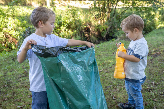 Enfants ramassant des bouteilles en plastique avec un sac poubelle dans une forêt — Photo de stock