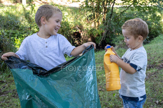 Voluntarios niños recogiendo botellas de plástico con una bolsa de basura - foto de stock