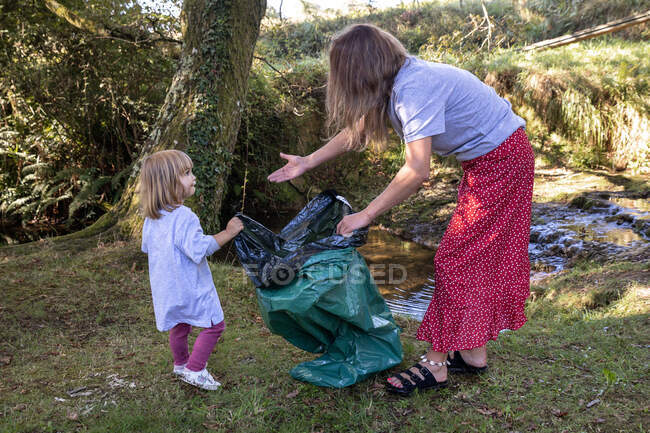 Volunteer mother with her daughter holding a garbage bag on the river — Stock Photo