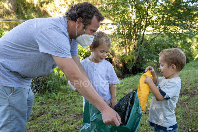 Отец коллекционирует пластиковые бутылки со своими детьми — стоковое фото