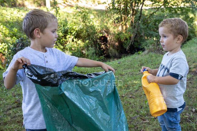 Дети собирают пластиковые бутылки с мешком для мусора в лесу, — стоковое фото