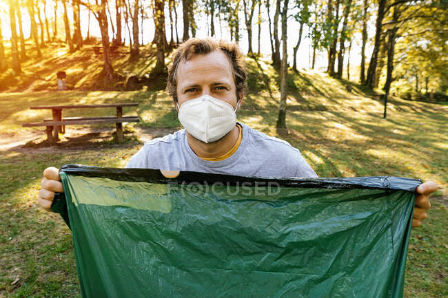 Волонтёр в медицинской маске держит мешок для мусора в лесу. — стоковое фото