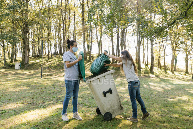 Mujeres voluntarias con máscaras médicas recogiendo basura en un bosque - foto de stock