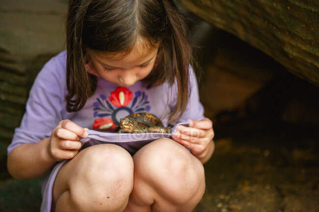 A little girl with dirty knees holds a small turtle on her lap — Stock Photo