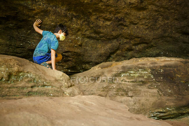 A boy crawls across boulders against rock wall in sandstone gorge — Stock Photo