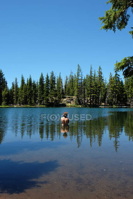 Hombre parado en un lago con reflejos de cuerpo, árboles y cielo - foto de stock