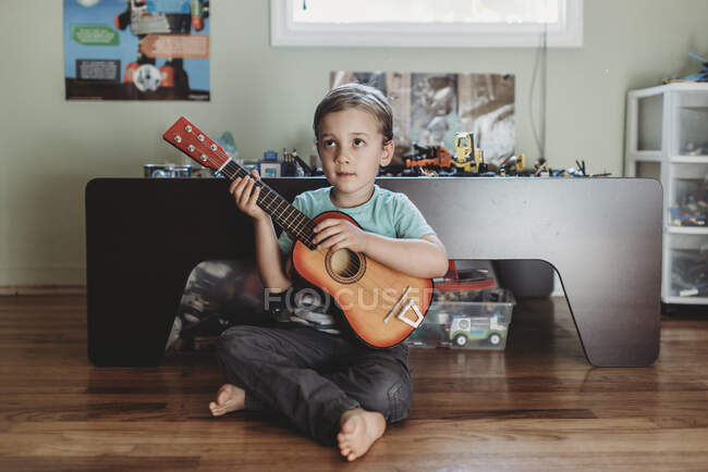 Pensivo menino sentado no chão de madeira com guitarra — Fotografia de Stock