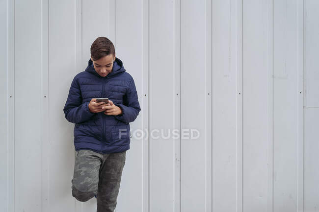 Adolescente con teléfono móvil en una pared blanca - foto de stock