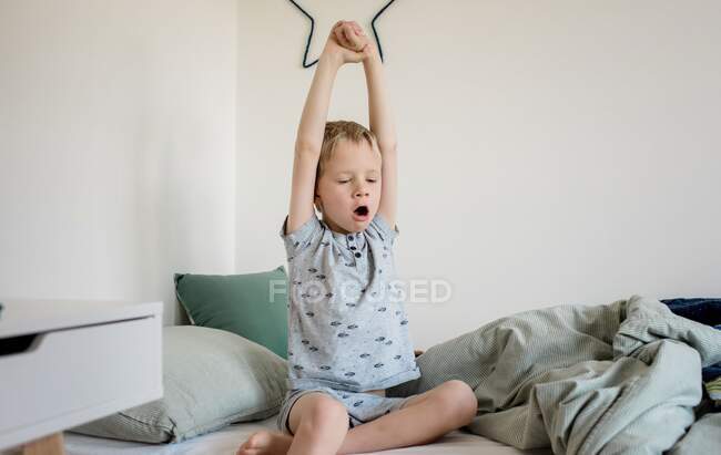 Jeune garçon se réveillant d'un sommeil et bâillant dans sa chambre — Photo de stock