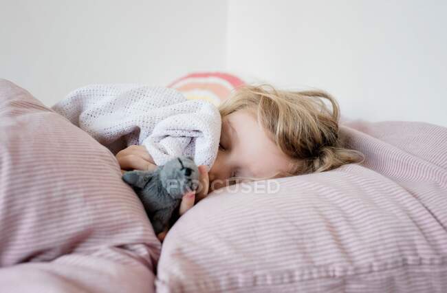 Jeune fille dormir dans son lit câliner ses jouets et couverture à la maison — Photo de stock