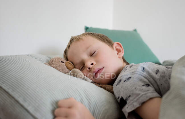Menino dormindo com seu urso na cama em casa — Fotografia de Stock