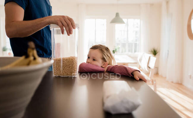 Девушка смотрит на свой завтрак, который ее отец держит на кухне — стоковое фото